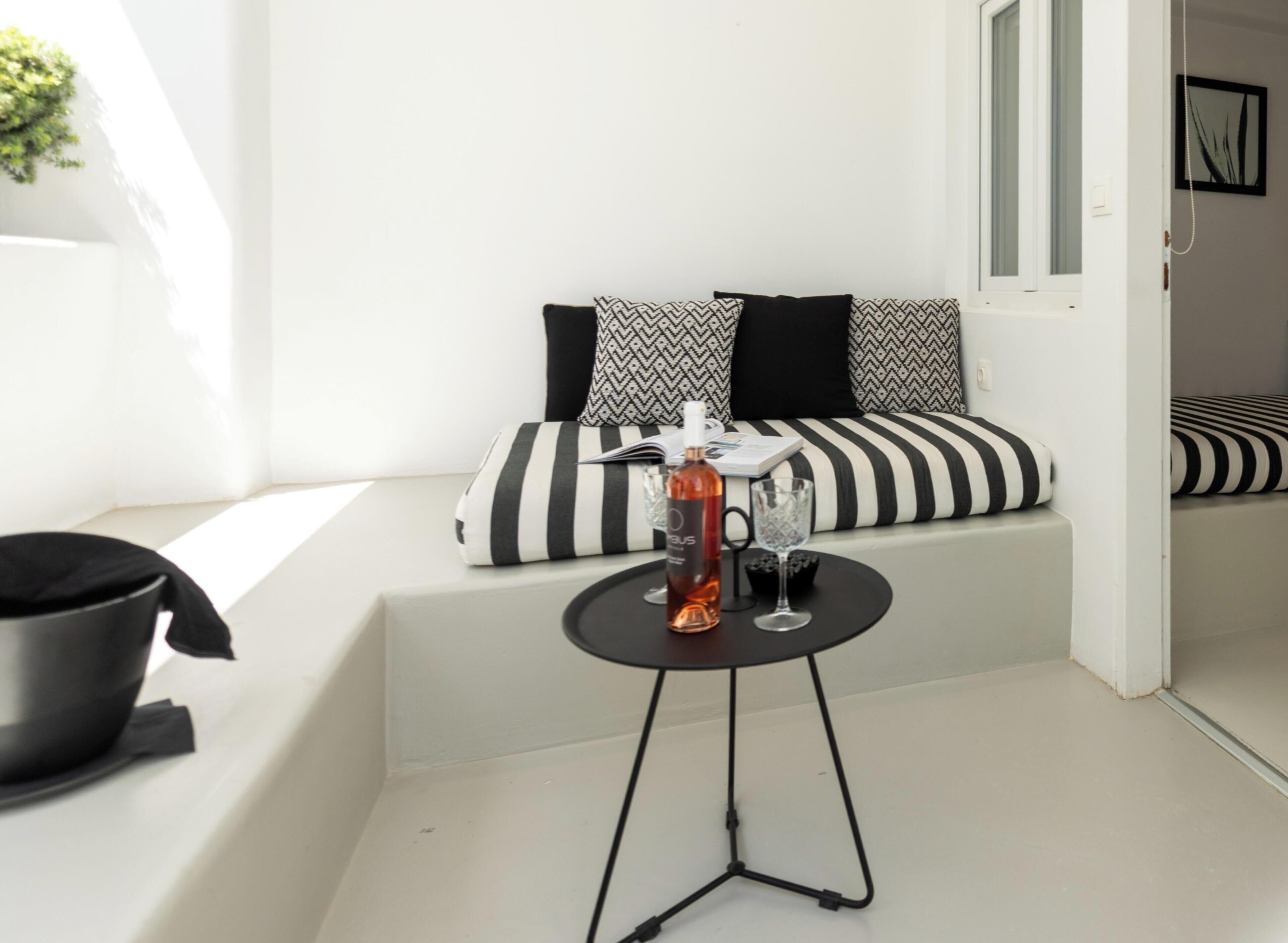 Una habitación minimalista con un sofá, una pequeña mesa con una botella y vasos, y una silla negra.