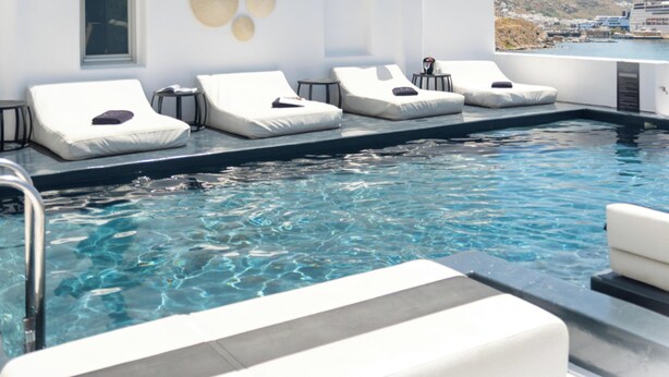 Une piscine à débordement située sur le toit, avec des chaises longues blanches et une vue dégagée sur la ville.