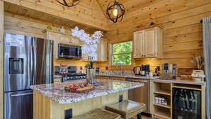 A modern kitchen with wooden cabinetry, stainless steel appliances, a granite countertop, and a central island with bar stools. - Ridge Hollow Retreat – Hot Tub, Fire Pit, Dogs (Gatlinburg)