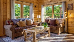 A cozy cabin interior with two sofas, a coffee table, and large windows offering a view of the outdoors. - Ridge Hollow Retreat – Hot Tub, Fire Pit, Dogs (Gatlinburg)