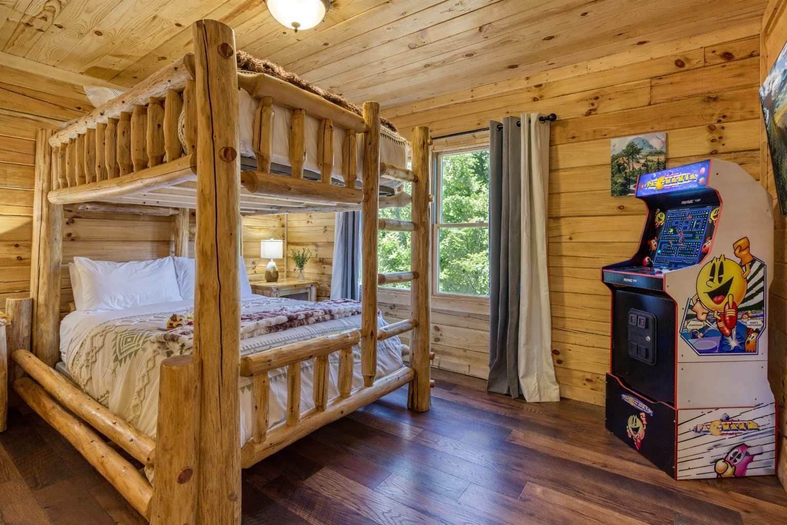 Et træhusværelse med køjeseng, et skrivebord med lampe, et vindue med gardiner og en Pac-Man arkademaskine.