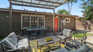 Eine überdachte Terrasse mit Gartenmöbeln, darunter ein Tisch und Stühle, sowie eine kleine Sitzgruppe mit einer Bank.