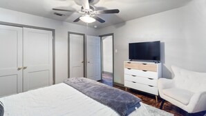 Ein Schlafzimmer mit Bett, Deckenventilator, Fernseher auf einer Kommode und einem Sessel.