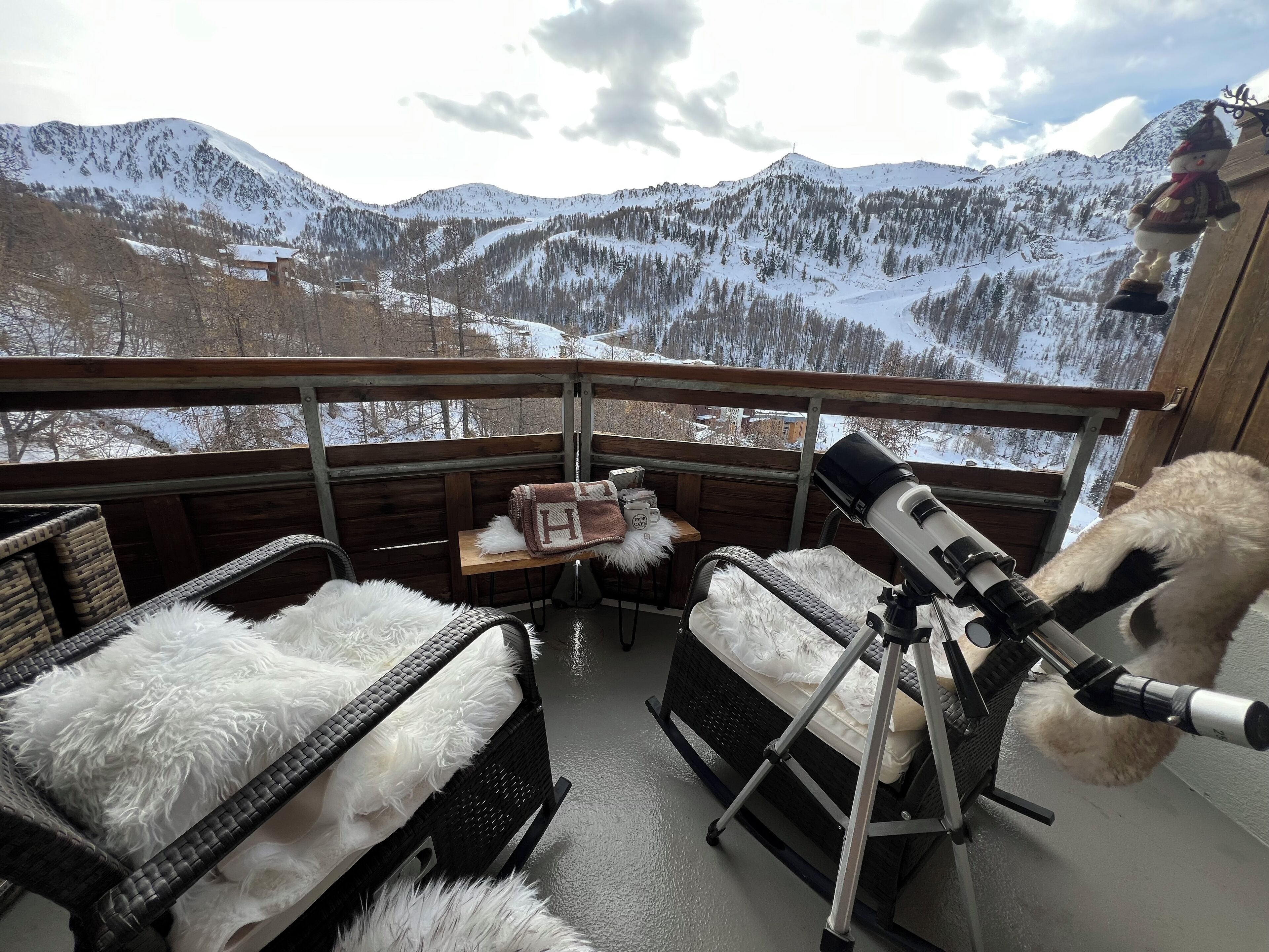 A balcony with a telescope, wicker furniture, and a view of snow-covered mountains.