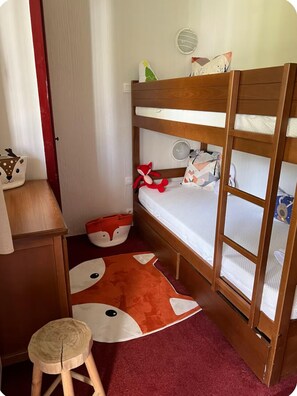 Una cama litera con un tapete rojo y blanco estampado, un taburete pequeño y un juguete en el suelo.