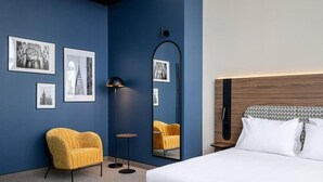 A hotel room with a bed, a yellow armchair, a floor lamp, and framed pictures on the wall. - B&B HOTEL Wrocław Old Town (Wrocław)