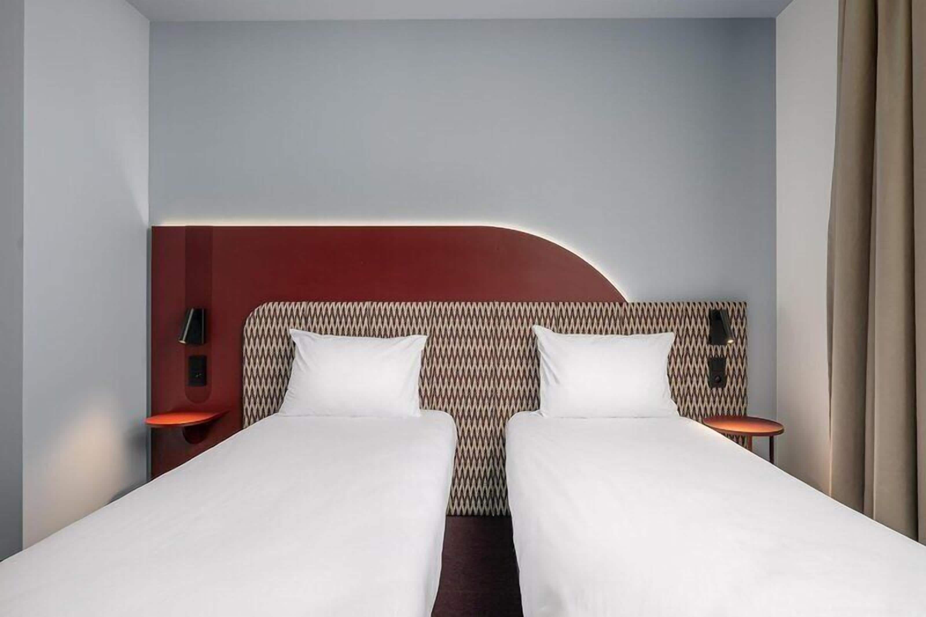 Habitación de hotel con diseño moderno, que presenta una cama grande con dos almohadas, un cabecero curvo y dos mesitas de noche con lámparas.