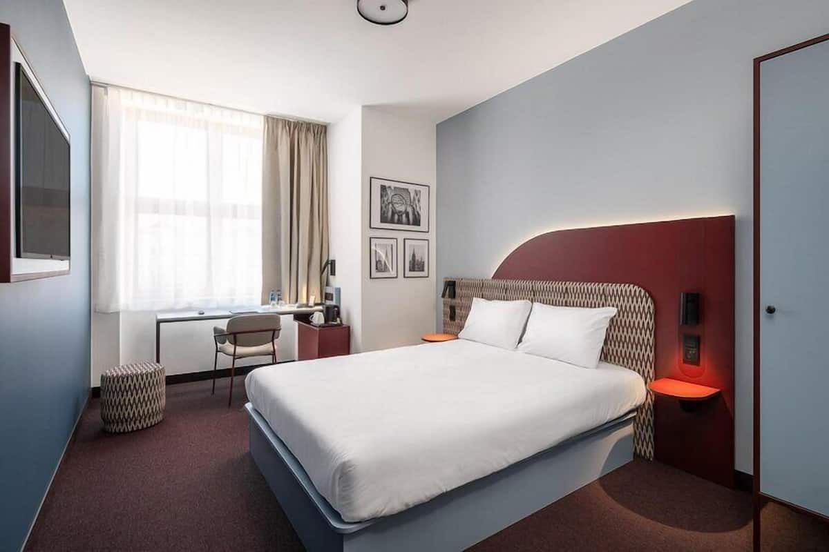 A hotel room with a bed, desk, chair, and a window with curtains.
