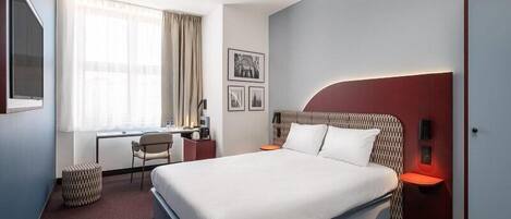 A hotel room with a bed, desk, chair, and a window with curtains.