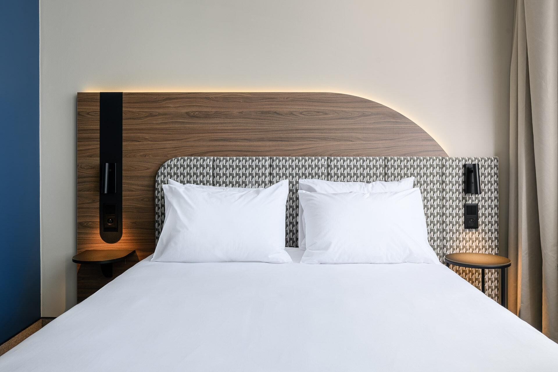 A neatly made bed with white linens, a houndstooth-patterned headboard, and a bedside table with a lamp.