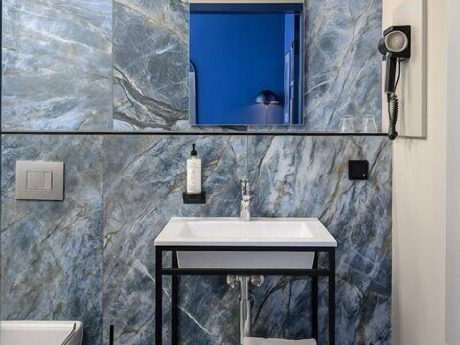 A bathroom with a marble wall, a sink, a mirror, a towel rack, and a handheld showerhead.