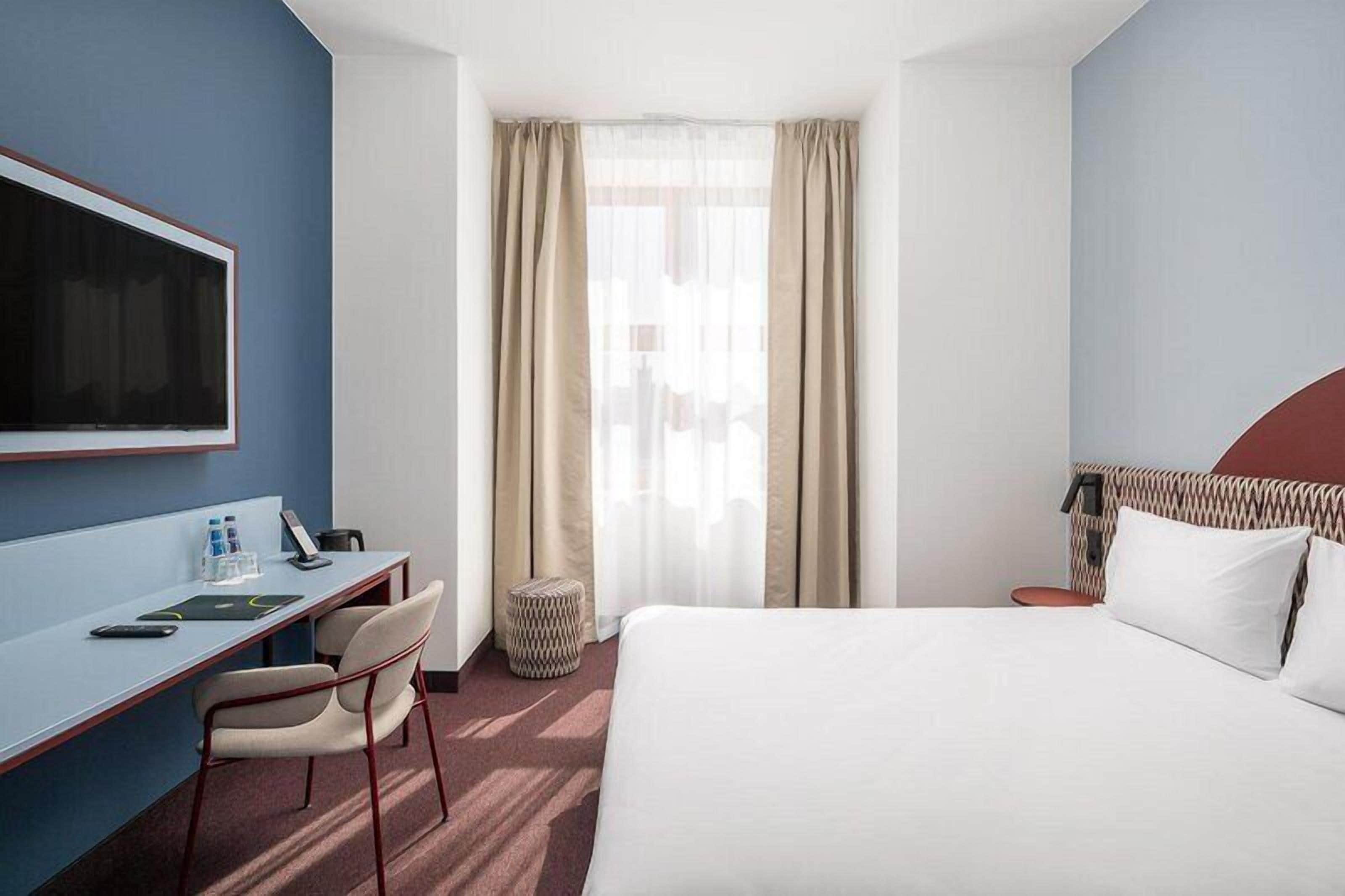 A hotel room with a bed, desk, chair, TV, and curtains.