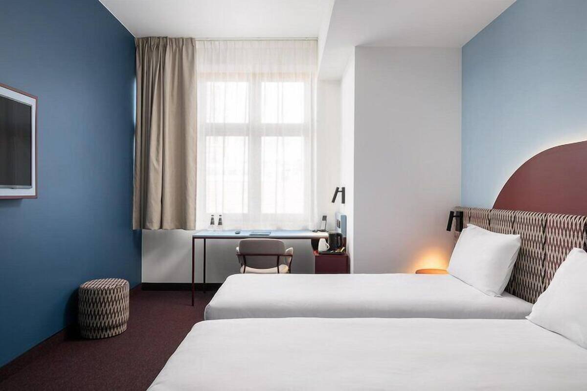 A hotel room with a bed, desk, chair, and a window with curtains.