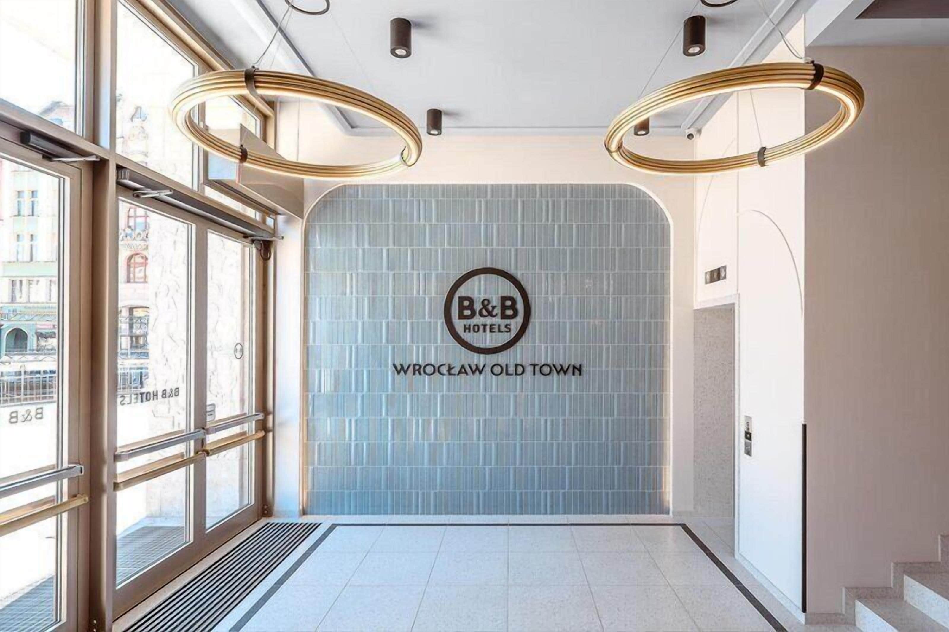 Un hall de hotel con ventanas amplias, el logotipo de un B&B y una pared de azulejos.