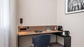A hotel room with a desk, chair, coffee maker, water bottles, and a framed picture on the wall.