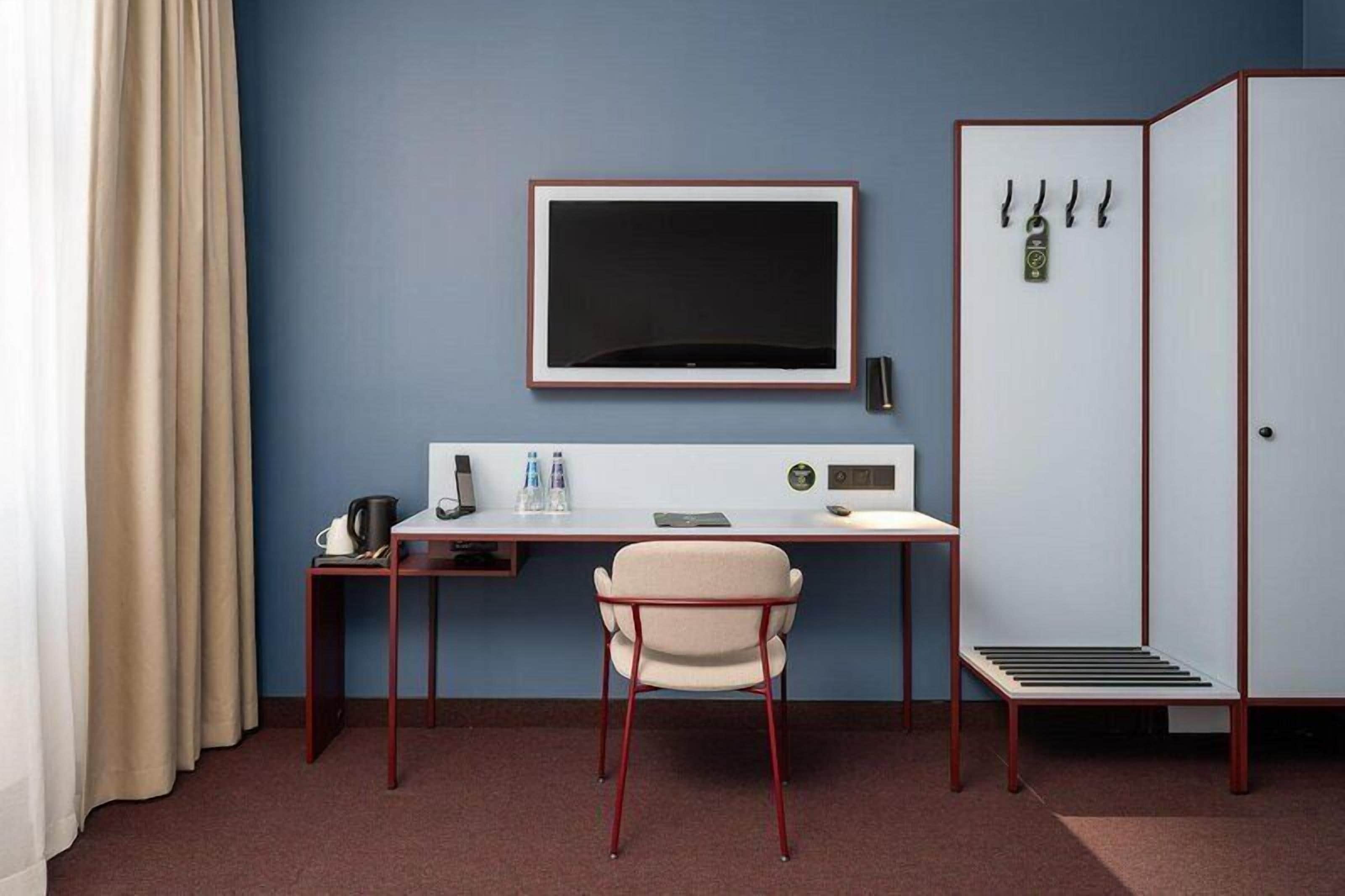Een hotelkamer met een bureau, stoel, kledingkast en een grote flatscreen-televisie.