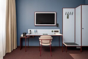Une chambre d’hôtel équipée d’un bureau, d’une chaise, d’une armoire et d’un grand téléviseur à écran plat.