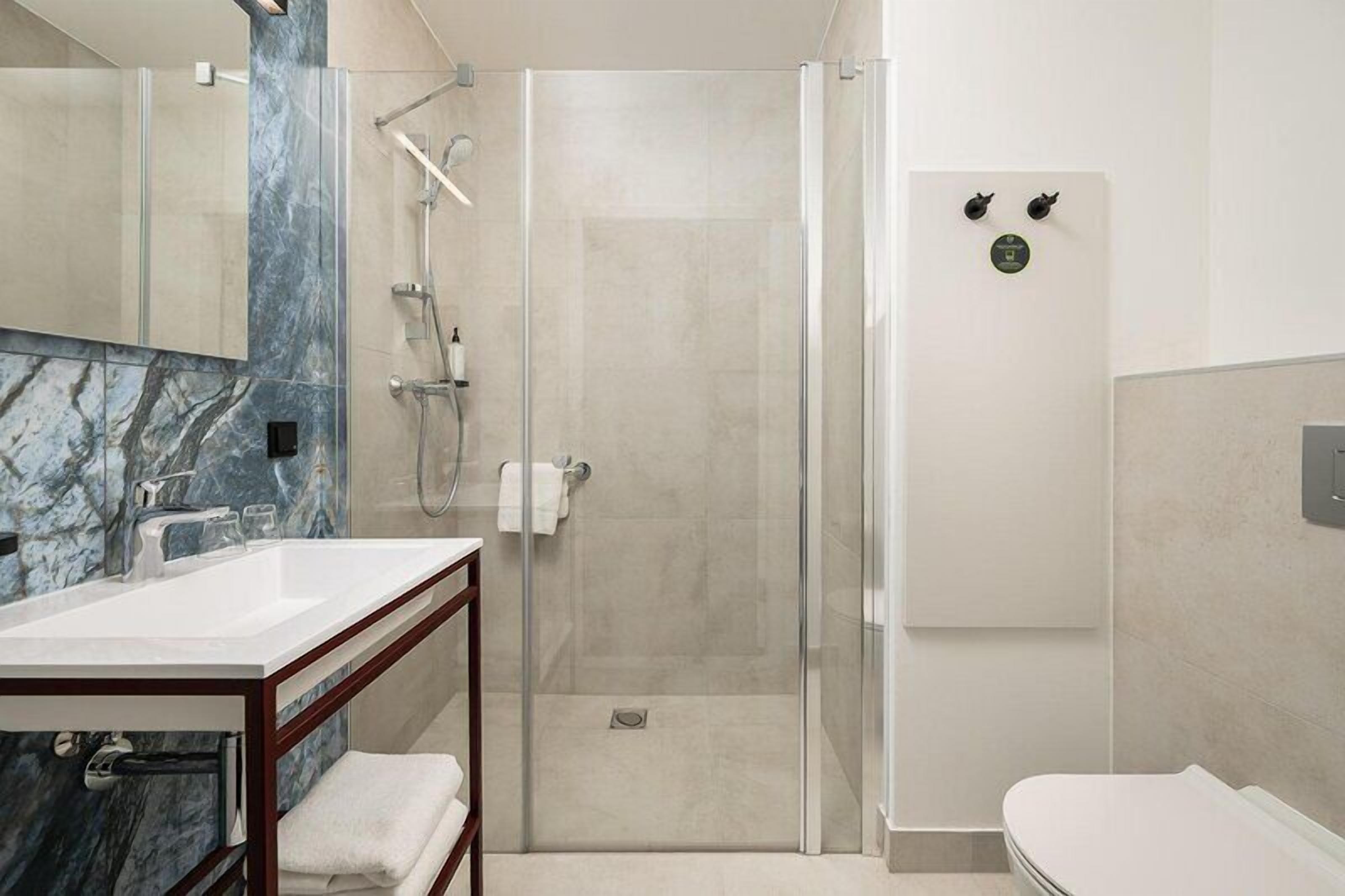 A modern bathroom with a glass-enclosed shower, a marble-topped sink, and a white toilet.