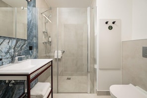 Un baño moderno con ducha de vidrio, tocador de mármol y retrete blanco.