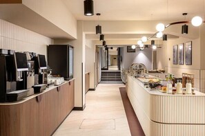 Un moderno vestíbulo de hotel con una recepción, máquinas de café y una zona de buffet.