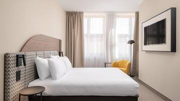 A hotel room with a bed, a round side table, a chair, a floor lamp, and a framed picture on the wall.
