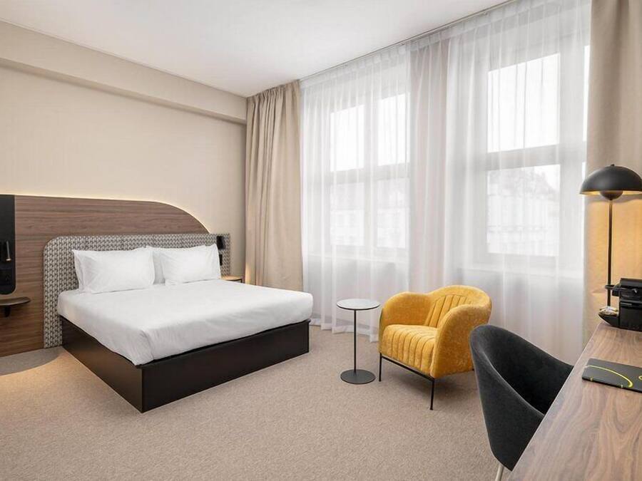 Una habitación de hotel con una cama, una mesita, una silla, un escritorio y una lámpara.