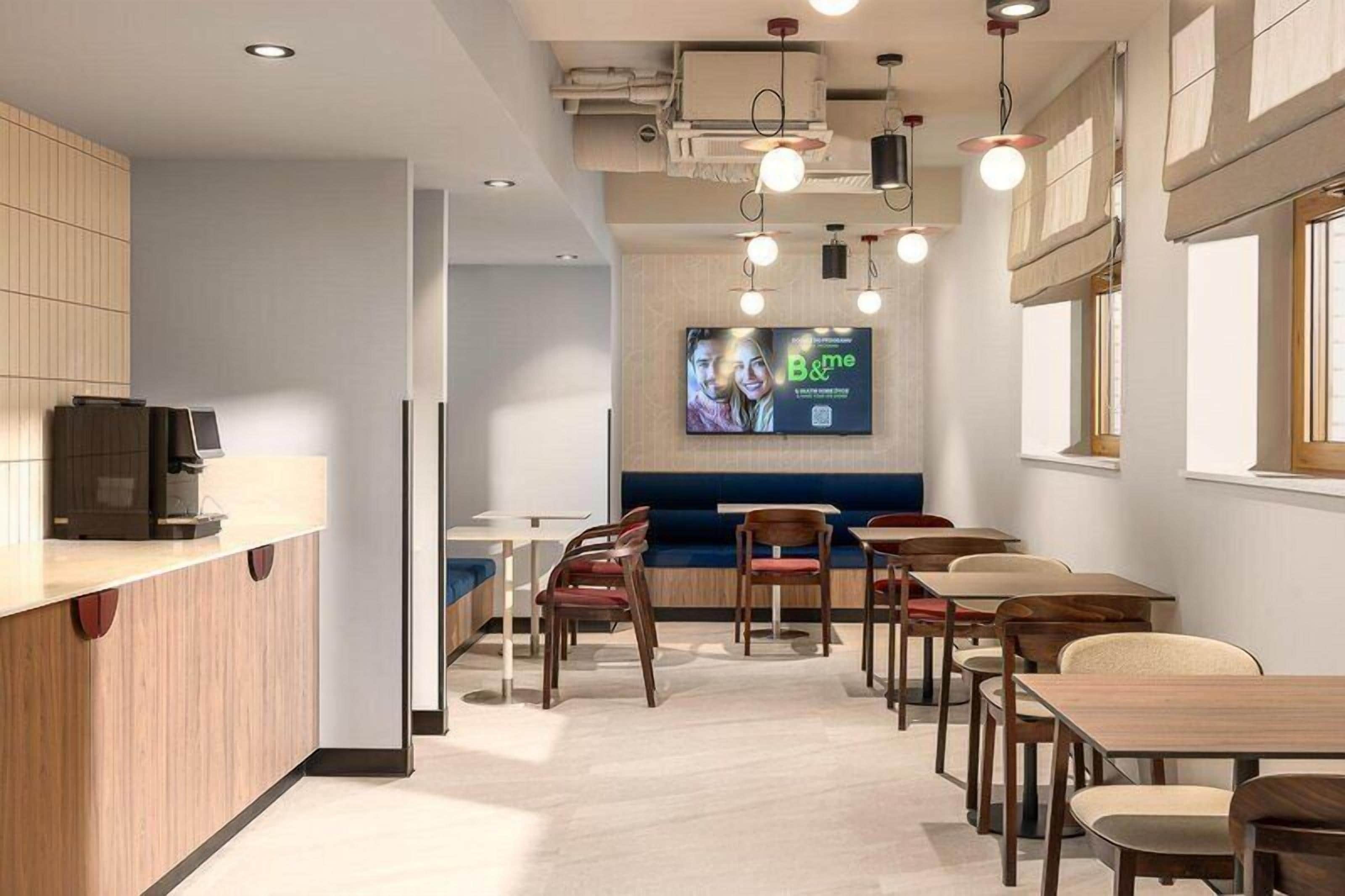 A modern hotel lobby with a reception desk, seating area, and a large screen displaying an advertisement.