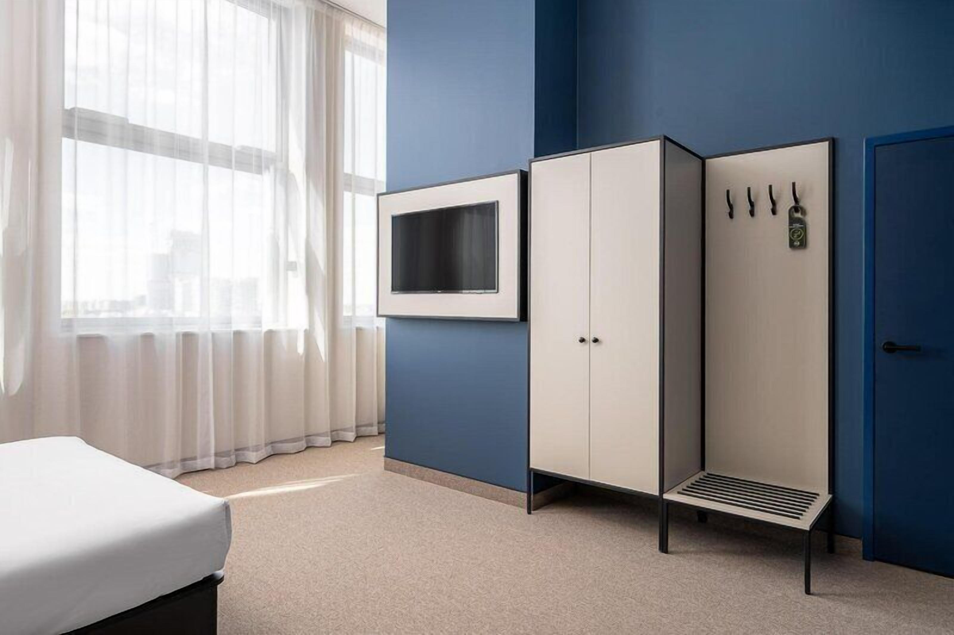 Une chambre avec un lit, un téléviseur fixé au mur, une armoire et une porte dotée d’une serrure.