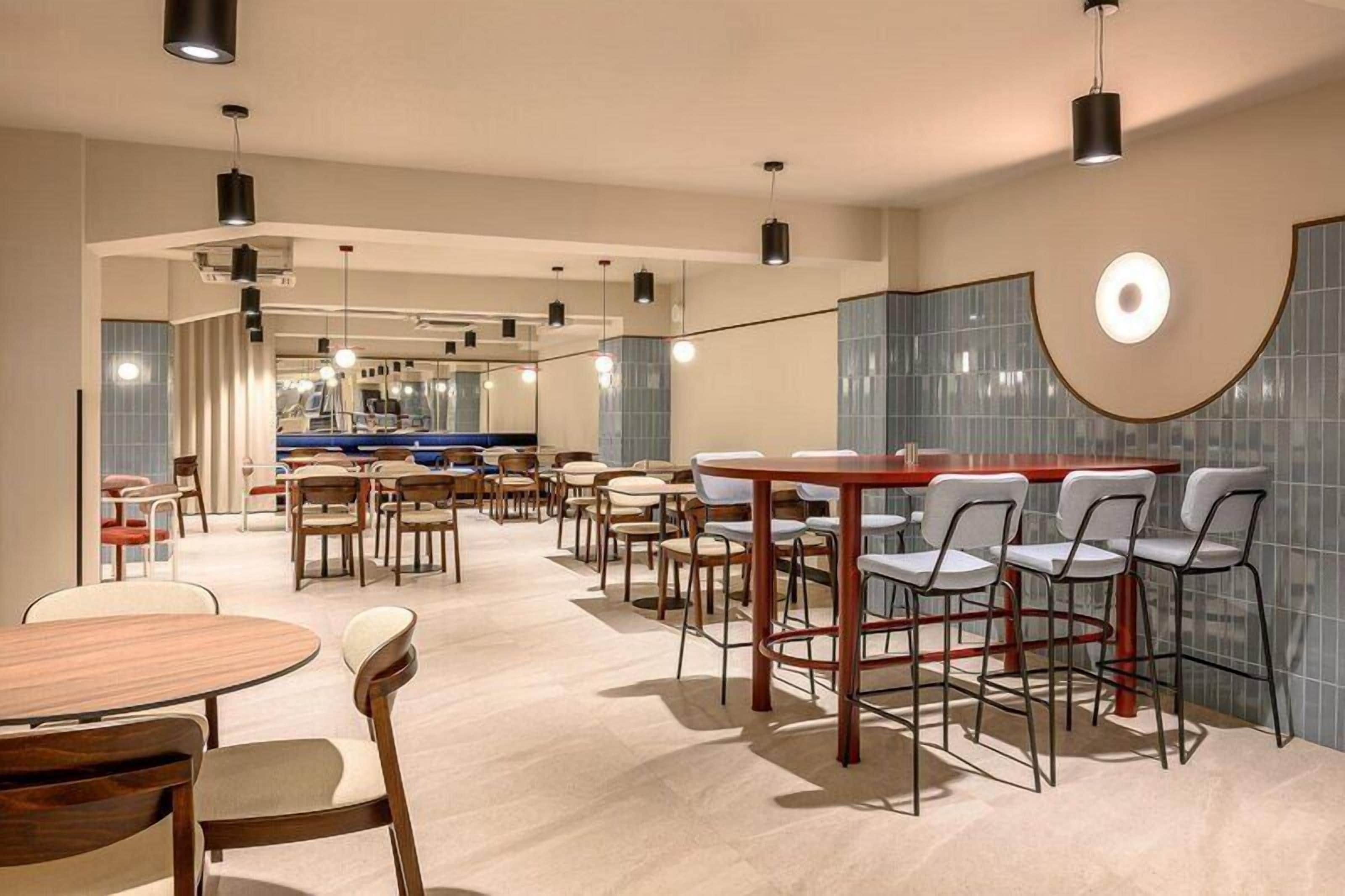 Un restaurante moderno con mesas y sillas redondas, una zona de bar y vistas a una piscina.