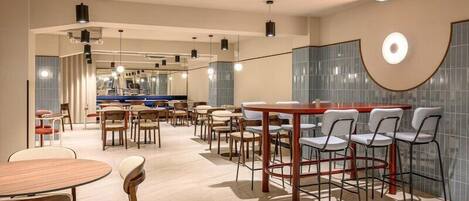 Un restaurante moderno con mesas y sillas redondas, una zona de bar y vistas a una piscina.