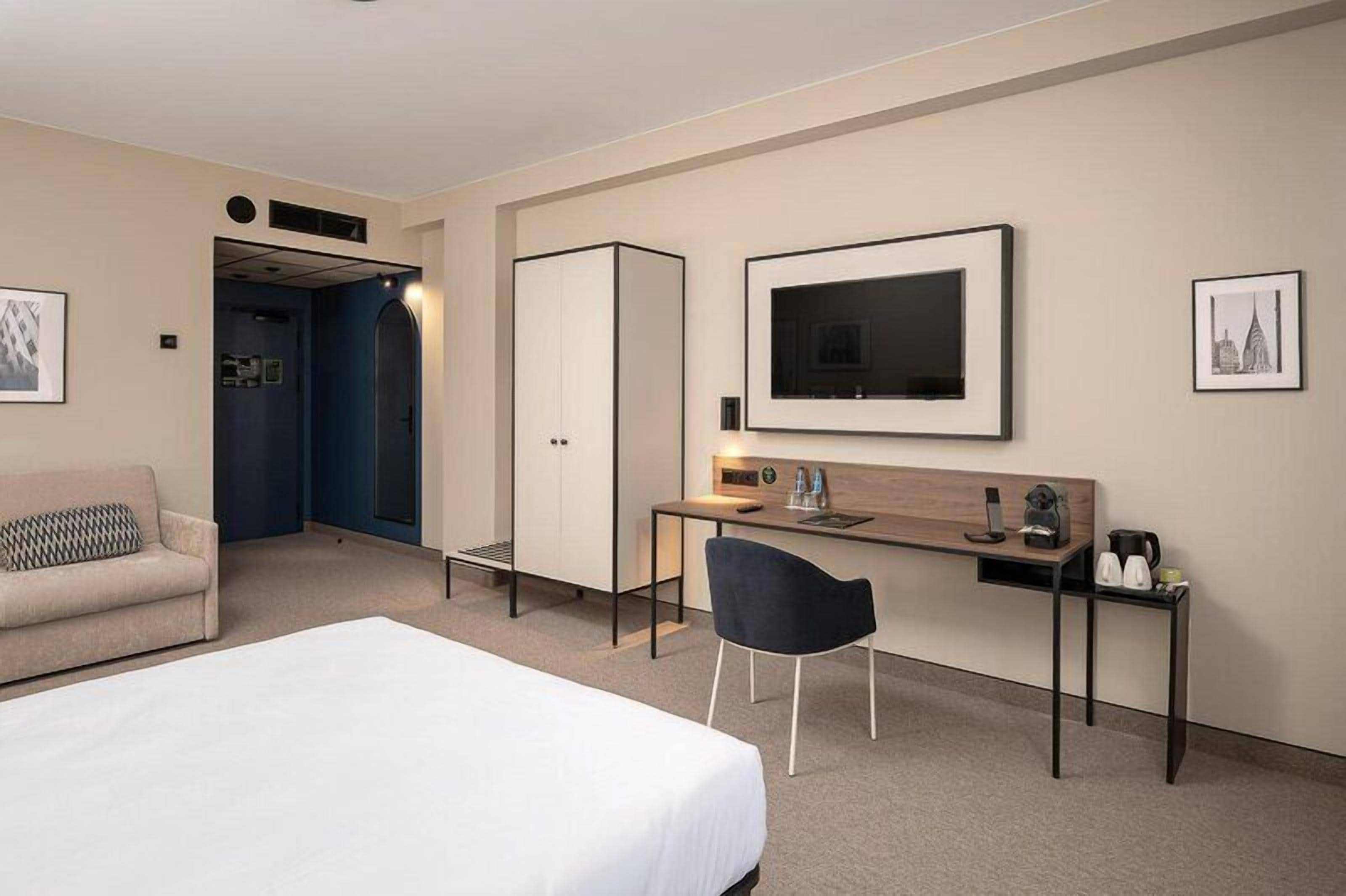 A hotel room with a bed, a desk, a chair, a wardrobe, and a television.