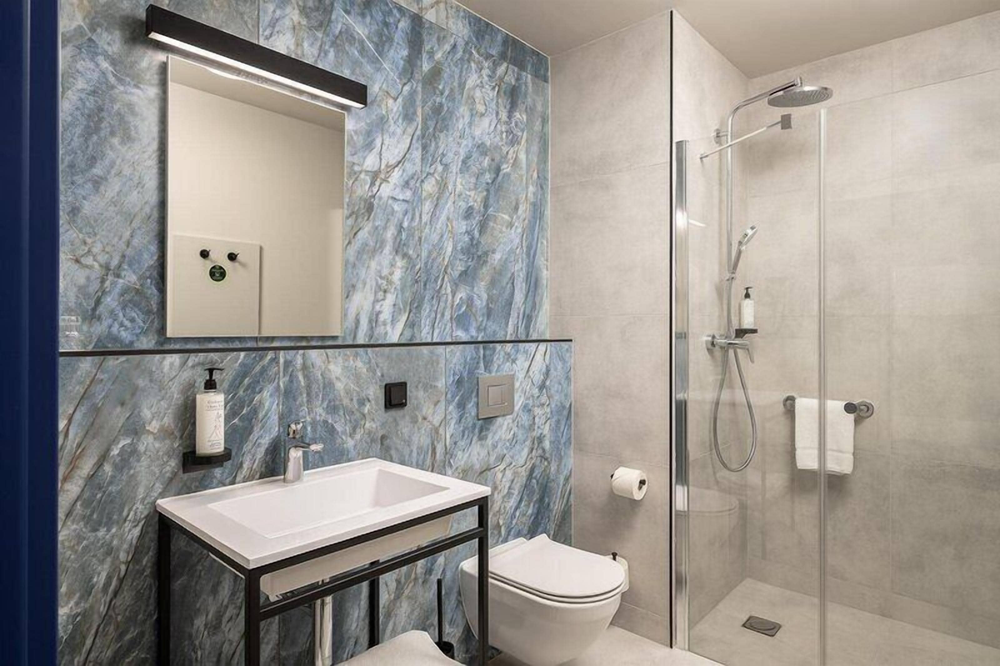 A bathroom with a marble wall, a sink, a toilet, and a glass-enclosed shower.