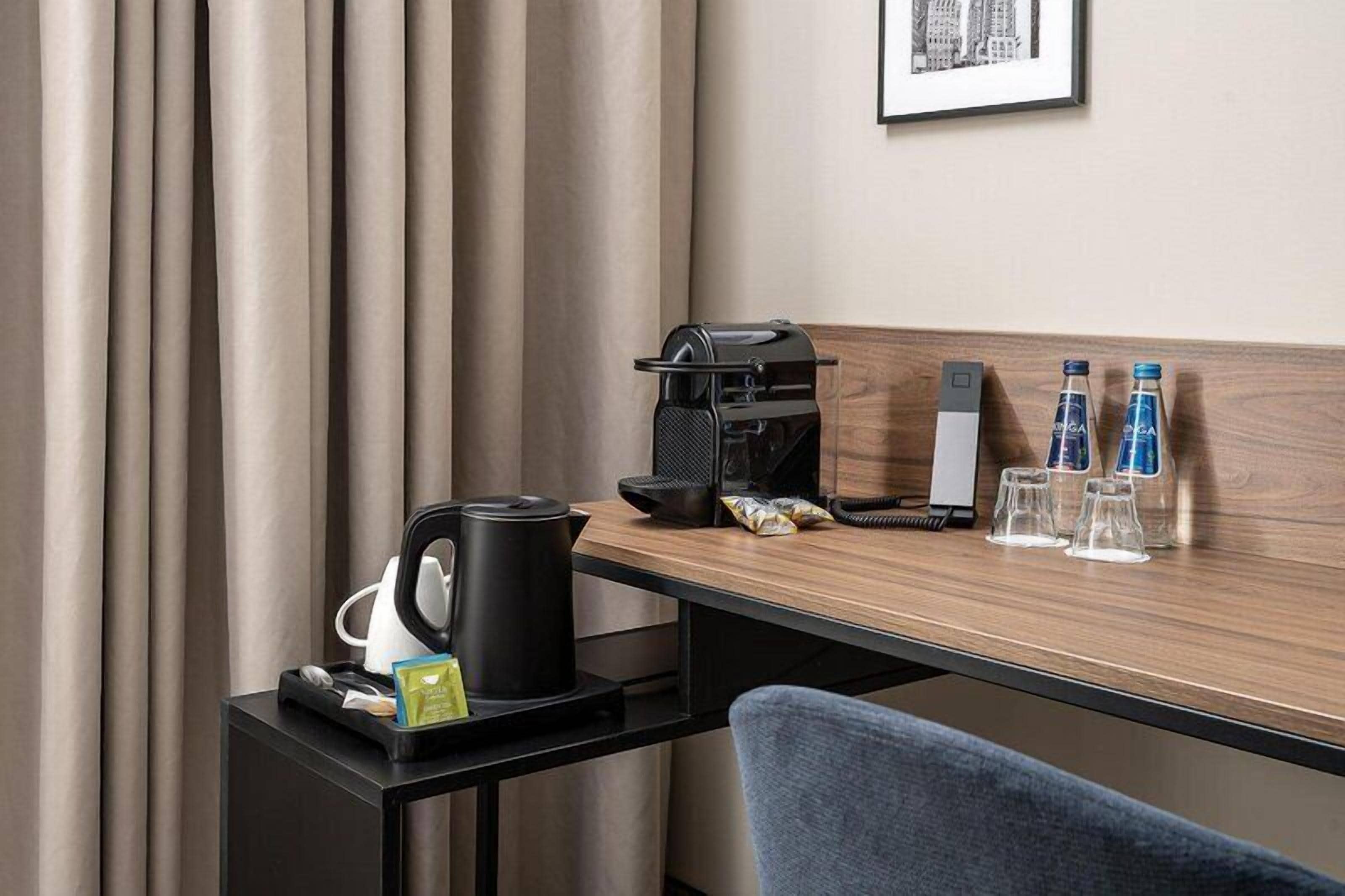 Habitación de hotel con escritorio de madera, cafetera, hervidor, teléfono y dos botellas de agua.