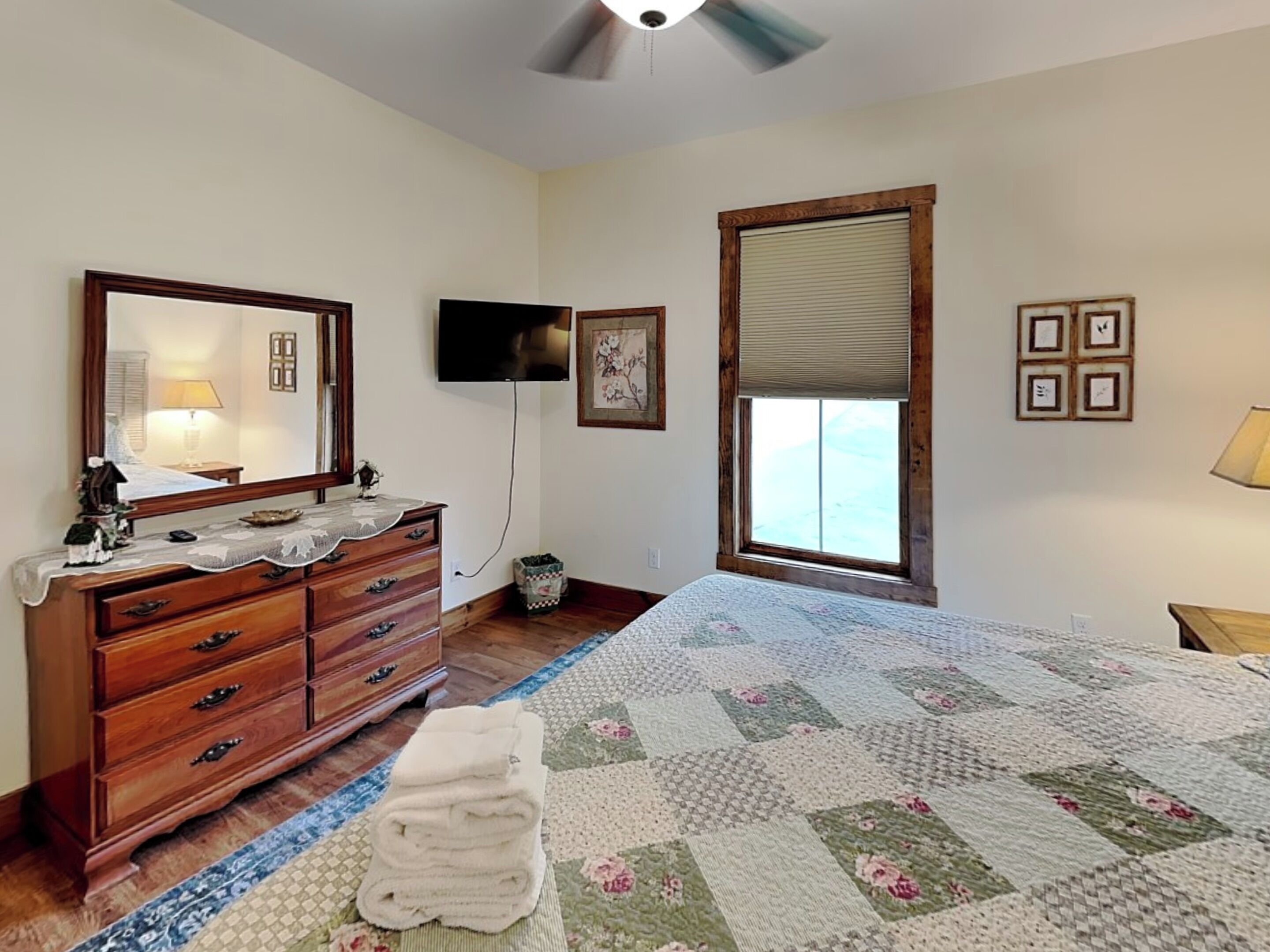 A bedroom with a bed, dresser, TV, window, and artwork.
