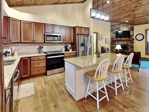 A modern kitchen with wooden cabinets, stainless steel appliances, and a central island with bar stools. - Buzzy Bee Lodge (McHenry)