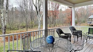 Une terrasse extérieure couverte, avec une table ronde et des chaises, une sphère décorative bleue, et une vue sur des arbres et un bâtiment en arrière-plan.