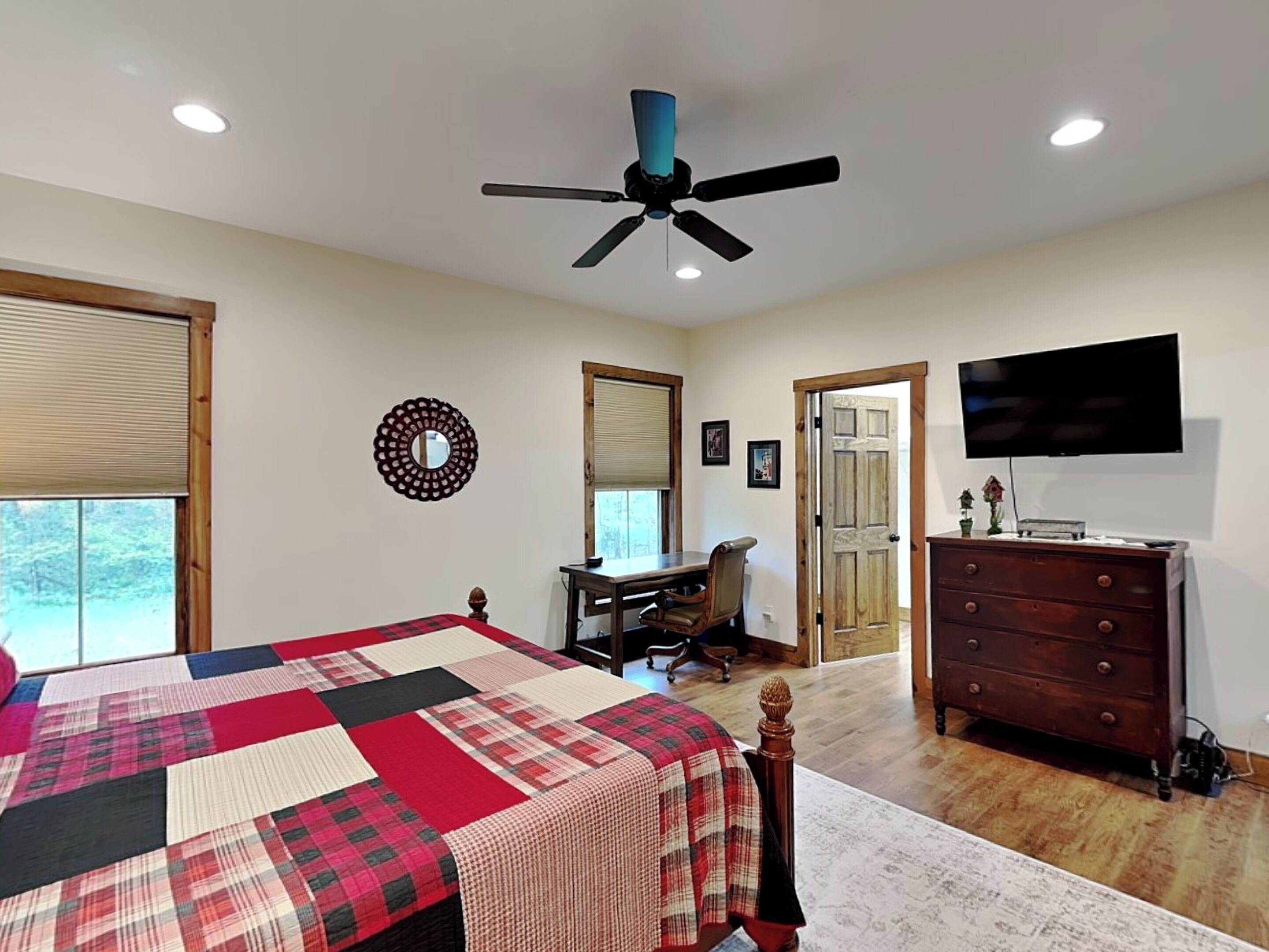 Une chambre à coucher comprenant un lit, un bureau, une chaise, une commode, un téléviseur et un ventilateur de plafond.