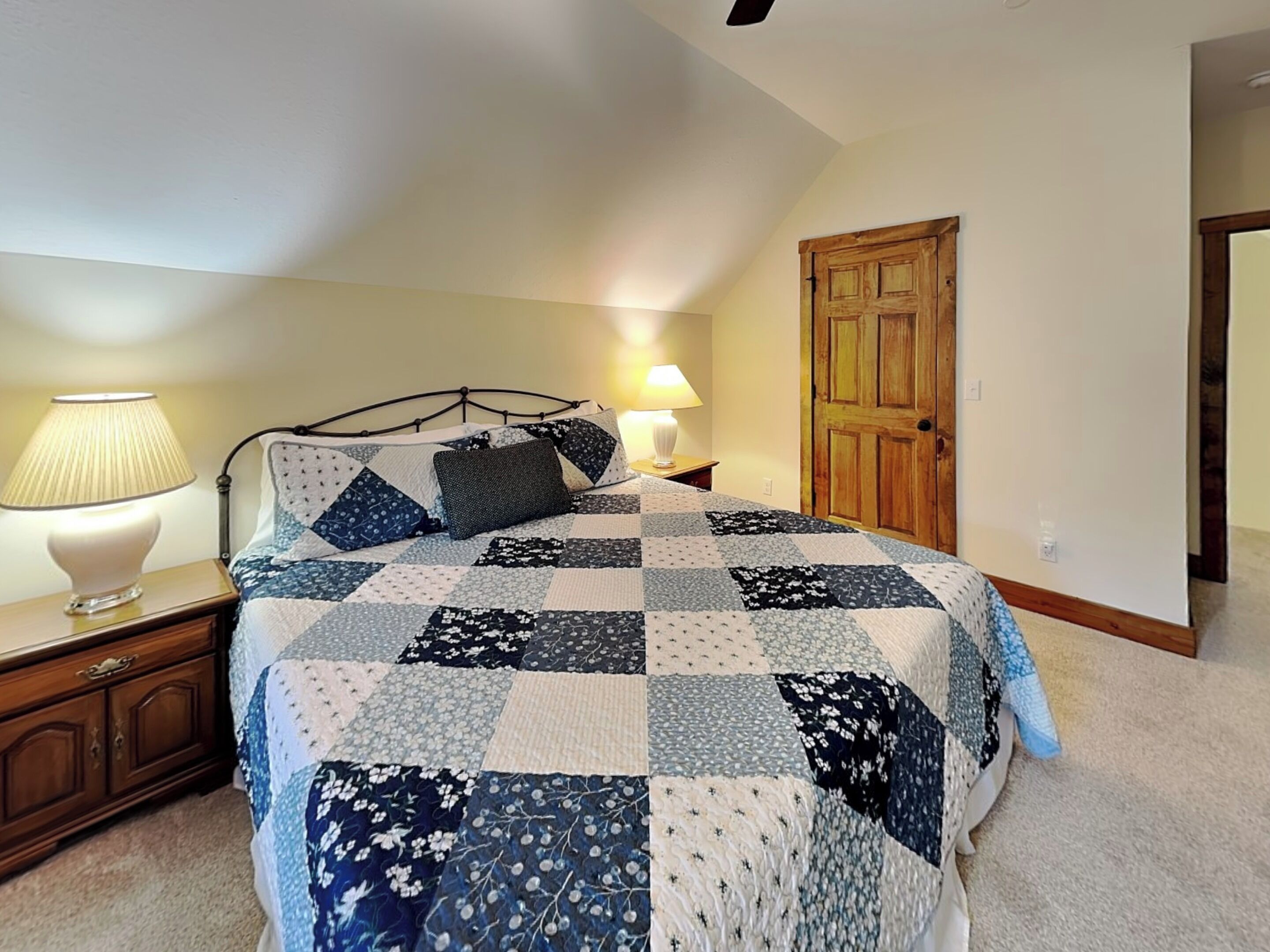A bedroom with a bed, two bedside lamps, a wooden door, and a carpeted floor.
