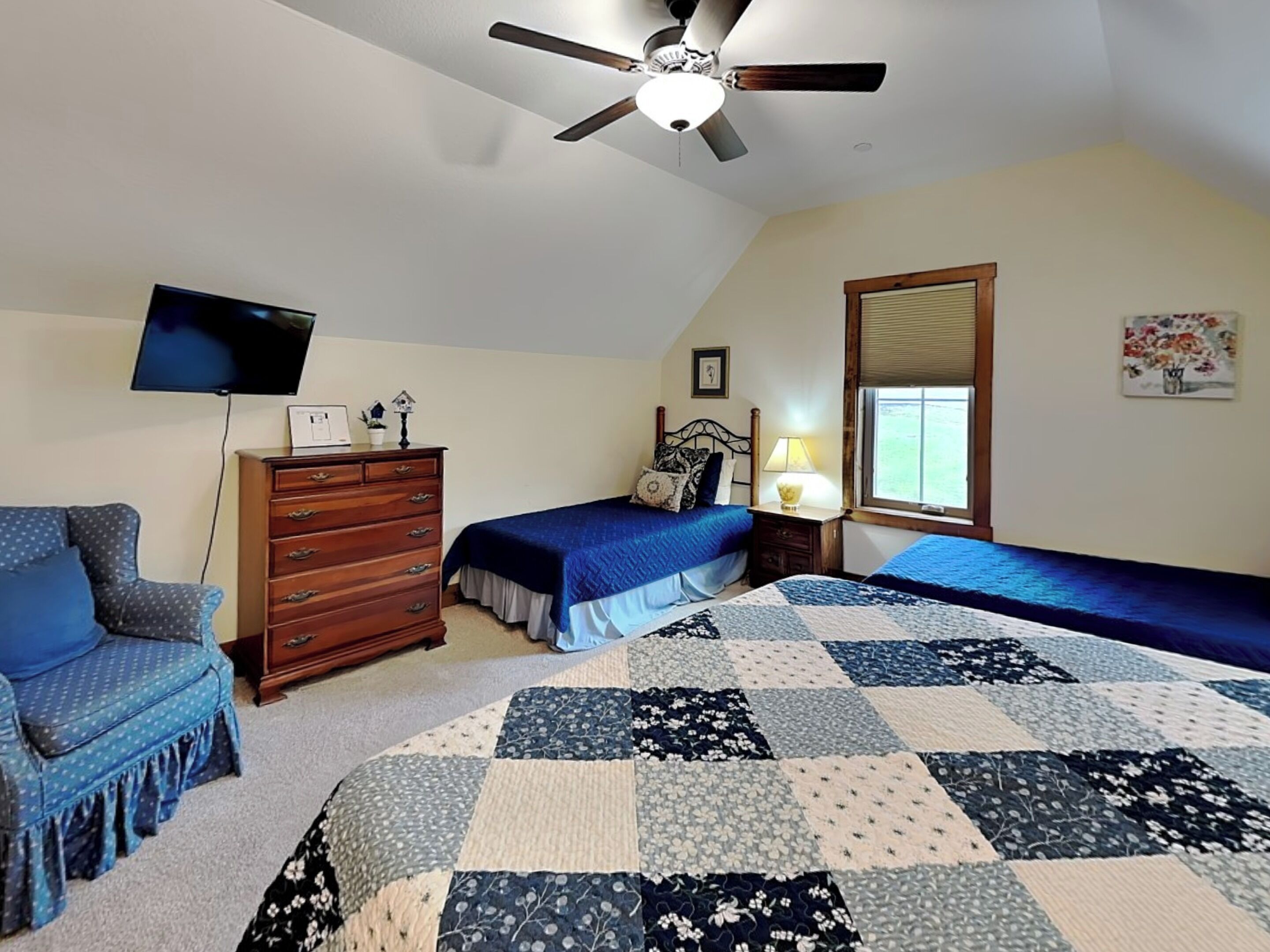 A bedroom with two beds, a ceiling fan, a TV, a dresser, and a window.