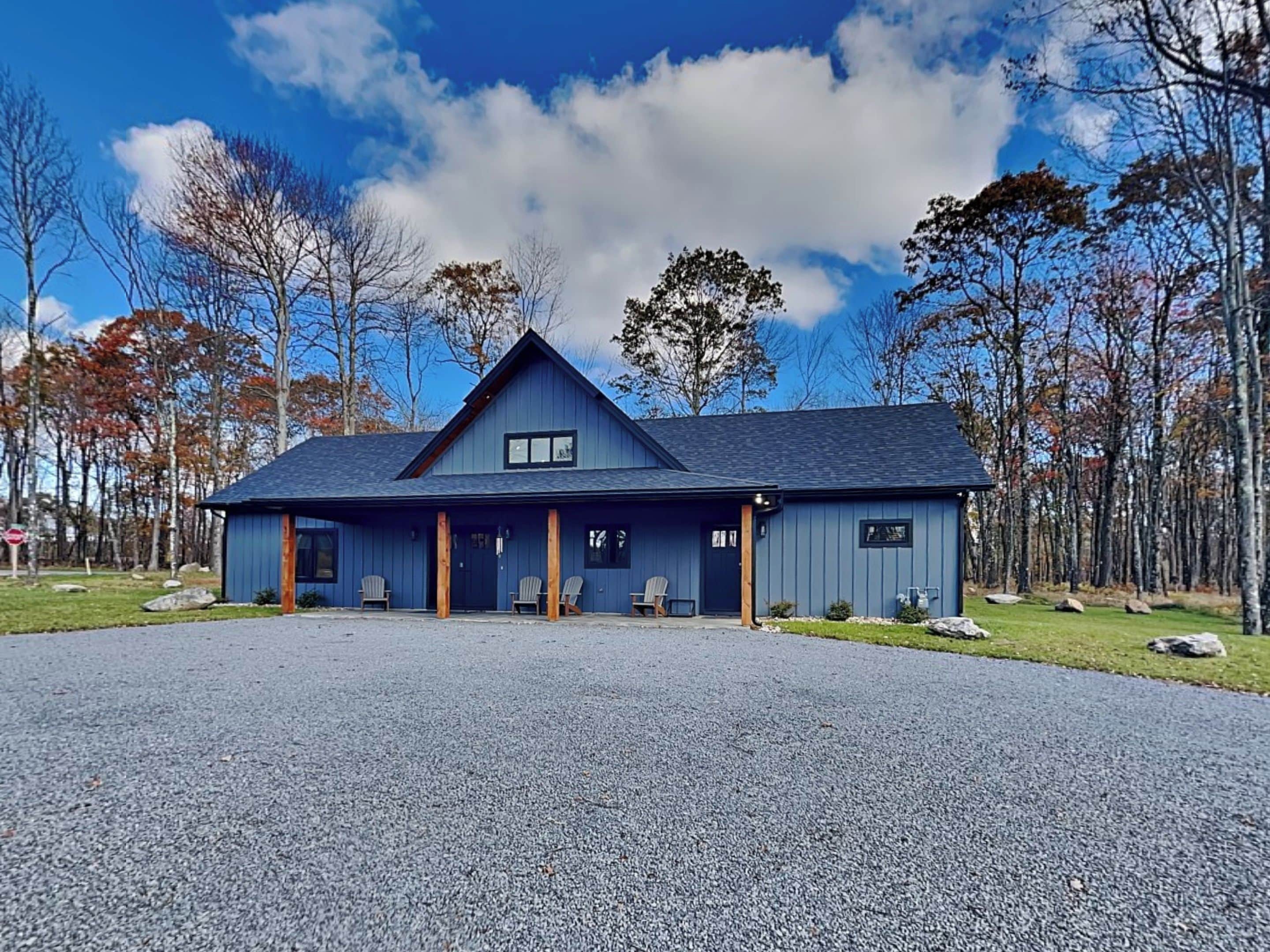 A two-story building with a dark blue exterior, a gabled roof, and a covered porch with four chairs.