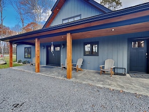 A modern building with a covered porch, two Adirondack chairs, and a black door. - Mountain Whisper (McHenry)