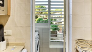 A laundry area with a washing machine, a drying rack, and a window with a view of greenery. - Apartment 'Villa Rocío' with Sea Views, Shared Pool and Wi-Fi (Calella de Palafrugell)