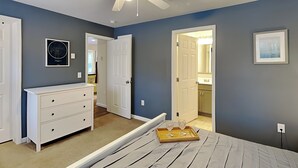 Un dormitorio con cama, cómoda, ventilador de techo y puerta que da a un baño.