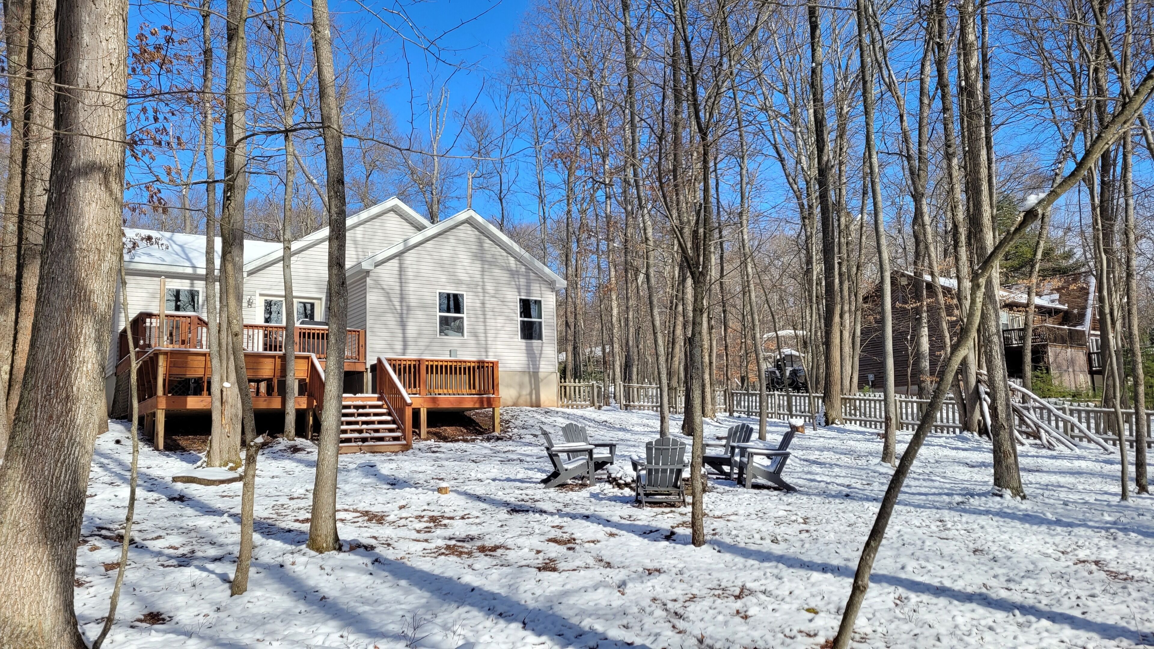 A cabin with a deck and outdoor seating area, surrounded by trees and snow.