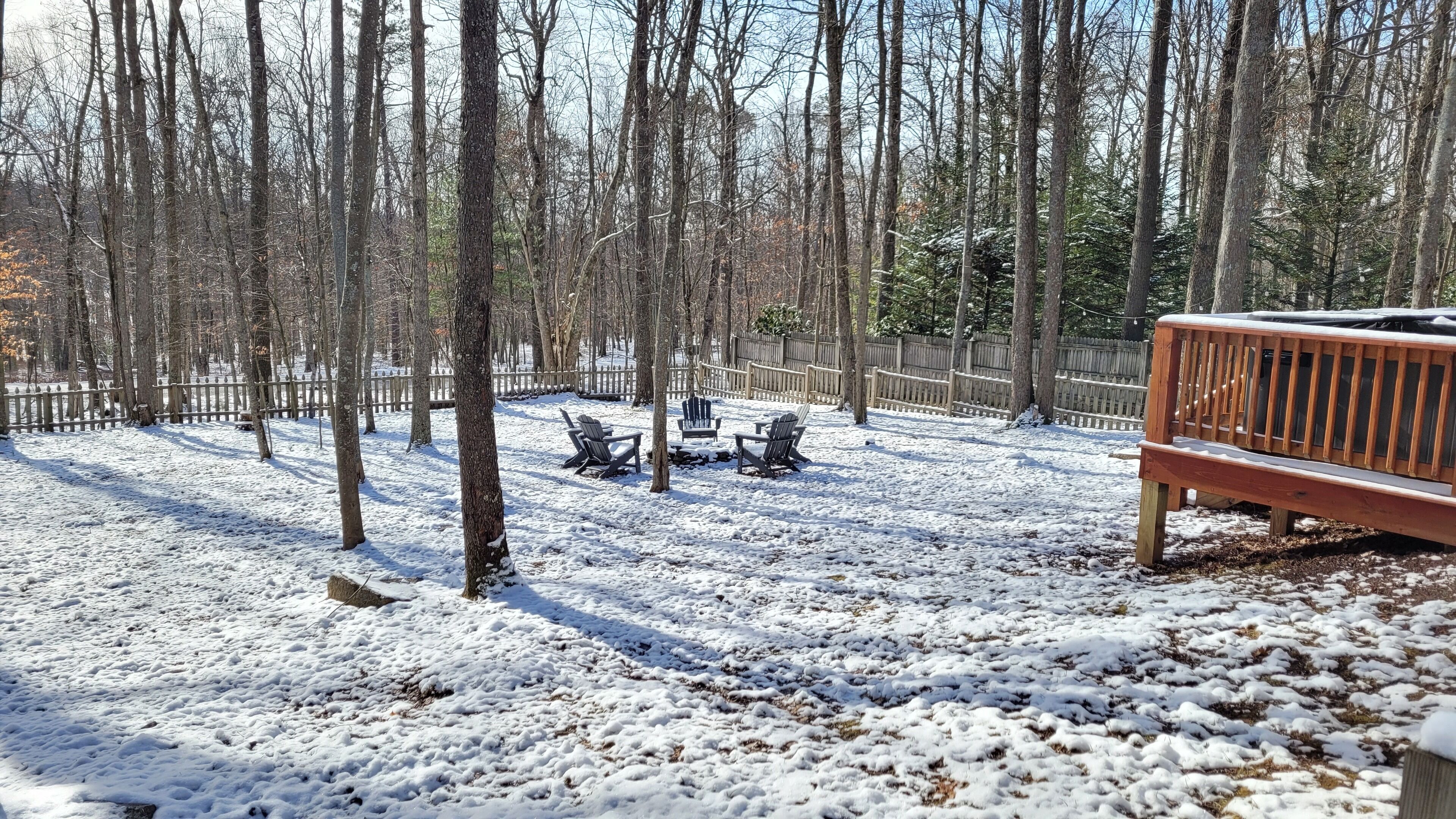 A snow-covered outdoor area with a wooden bench and Adirondack chairs.