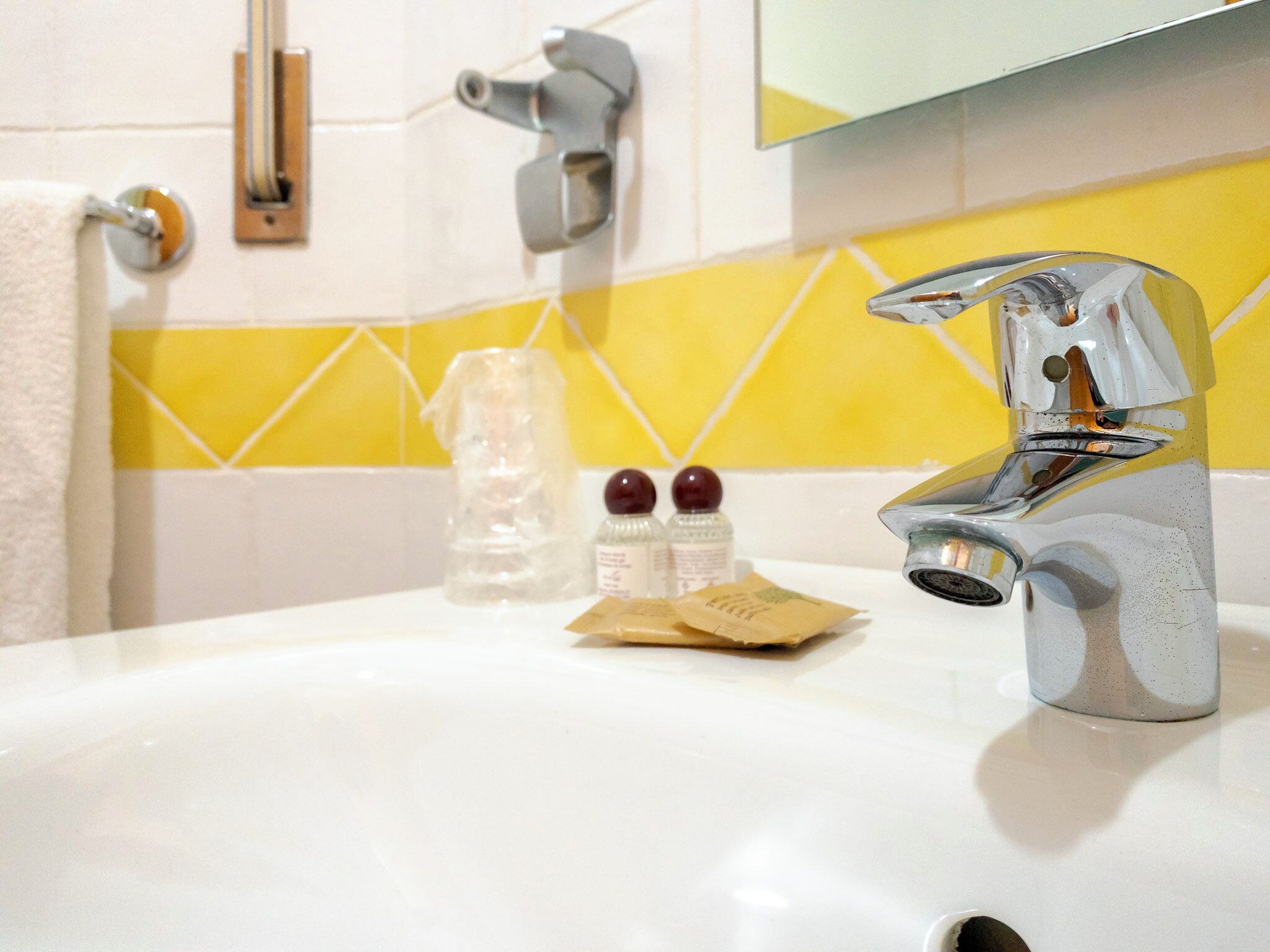 Un lavabo de salle de bain avec un robinet chromé, un pare-éclaboussures carrelé de jaune et de blanc, et un miroir au-dessus du lavabo.