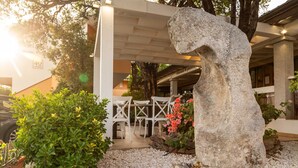 A stone sculpture in a garden area with a building in the background. - hotel ristorante Donatella (Posada)