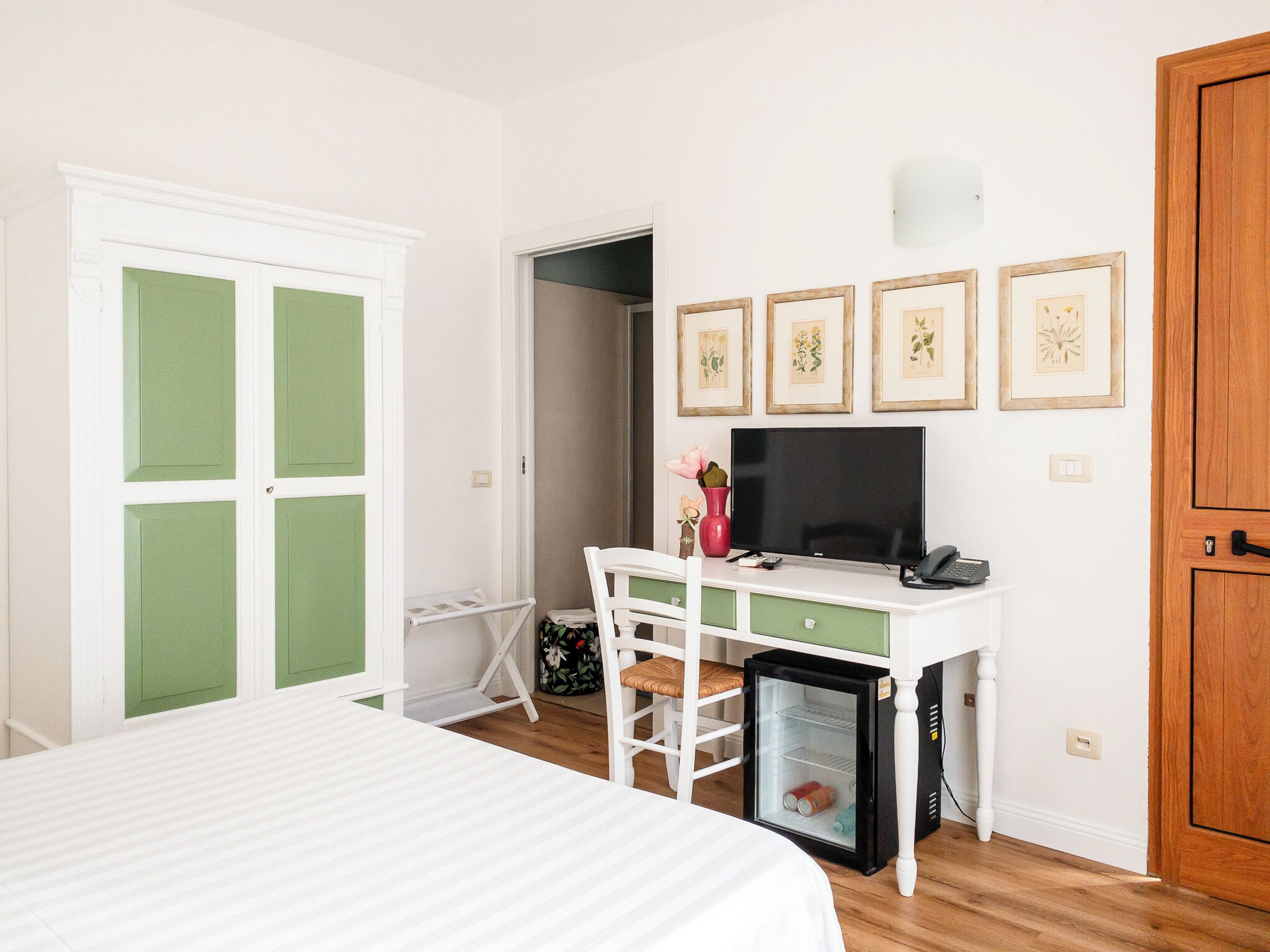 A bedroom with a bed, a desk with a computer, a small fridge, and a door with green panels.