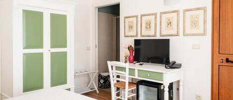 A bedroom with a bed, a desk with a computer, a small fridge, and a door with green panels.