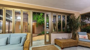 A hotel lobby with wicker furniture, a reception desk, and a door leading to the outside. - hotel ristorante Donatella (Posada)